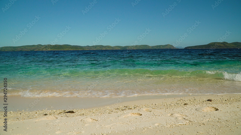 Sandy beach on the island and waves rolling on the coastline. Malajon Island, Philippines, Palawan. Summer and travel vacation concept.