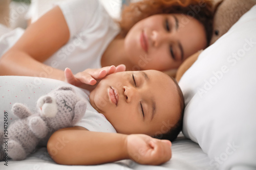 Young African-American woman and her sleeping baby on bed