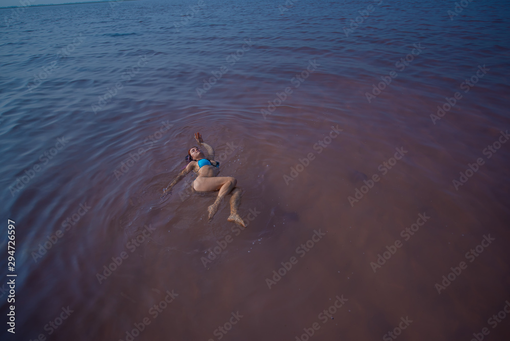 A woman in a blue bikini swims on her back in a salt lake. Miracle of