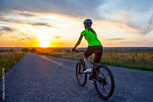 Beautiful girl cyclist rides a bicycle on the road in the sunset.