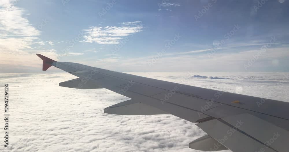 View of wing and engine of aeroplane from interior cabin through window over thick layer of cloud. Cloudscape from airline during morning journey.