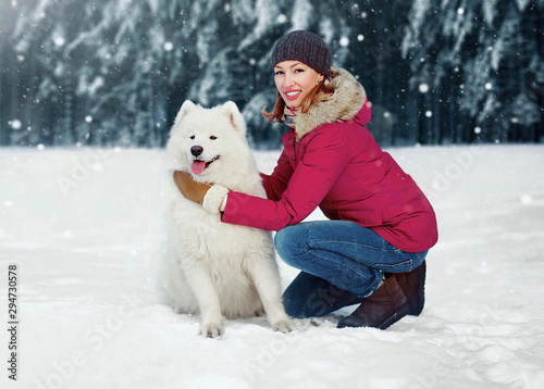 Winter portrait cheerful smiling owner woman hugging white Samoyed dog while sitting on snow walking in snowy park © guas
