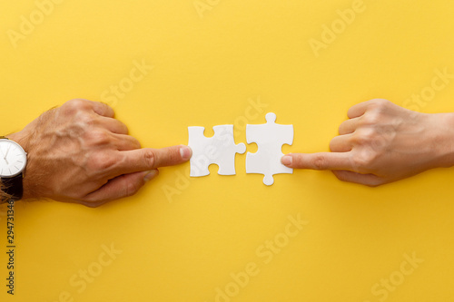 cropped view of woman and man matching pieces of white jigsaw puzzle on yellow background photo