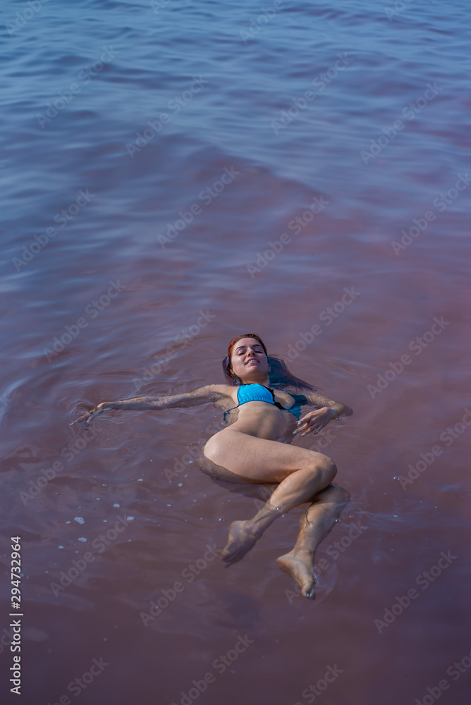 A woman in a blue bikini swims on her back in a salt lake. Miracle of nature pink lake. Deposit and extraction of salt. Dense water pushing to the surface. Therapeutic procedures in mineral water.