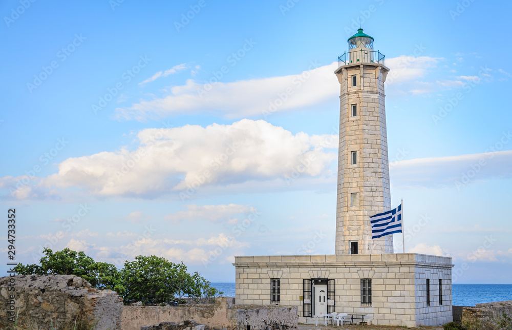 A lighthouse with a greek flag against a cloudy blue sky in Gytheio Greece