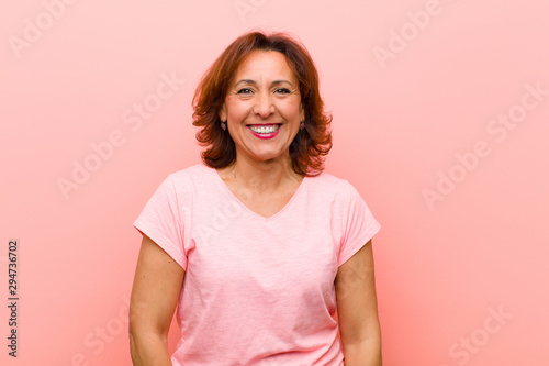 middle age woman looking happy and goofy with a broad, fun, loony smile and eyes wide open against pink wall photo