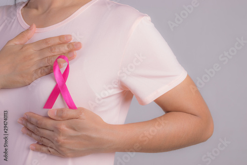 Closeup of pink badge ribbon on woman chest to support breast cancer cause. Healthcare, medical and breast cancer awareness concept.