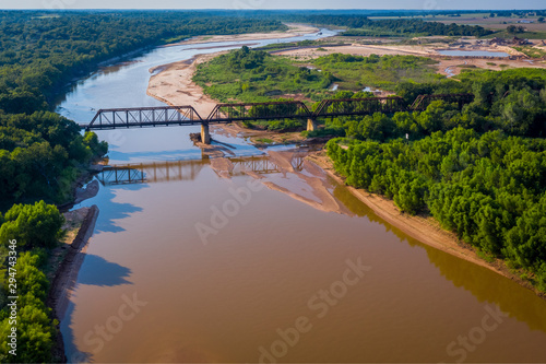 Aerial photo of Train trestle crossing muddy river that winds into the landscape on the Texas and Oklahoma border | Train tracks crossing river photo