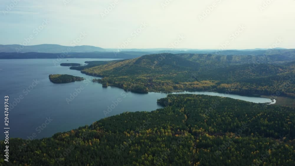 Aerial panoramic view of Turgoyak national park with beautiful pure water of lake and relict forest with pines, birches; autumn sunny evening with colorful foliage of deciduous trees; famous landmark Aerial panoramic view of Turgoyak national park with beautiful pure water of lake and relict forest with pines, birches; autumn sunny evening with colorful foliage of deciduous trees; famous landmark