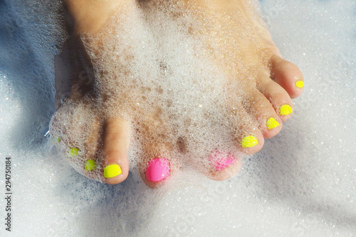 Fototapeta Naklejka Na Ścianę i Meble -  Female legs with bright yellow and pink varnish in a foam bath. In bright sunshine. The shadows...