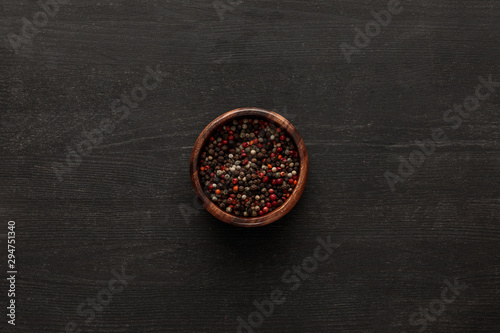 top view of brown bowl with whole peppercorns on dark wooden surface with copy space