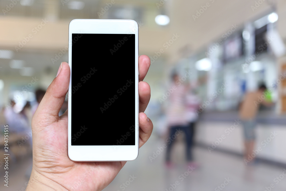 Hand of a man holding smartphone device on blur hospital background.