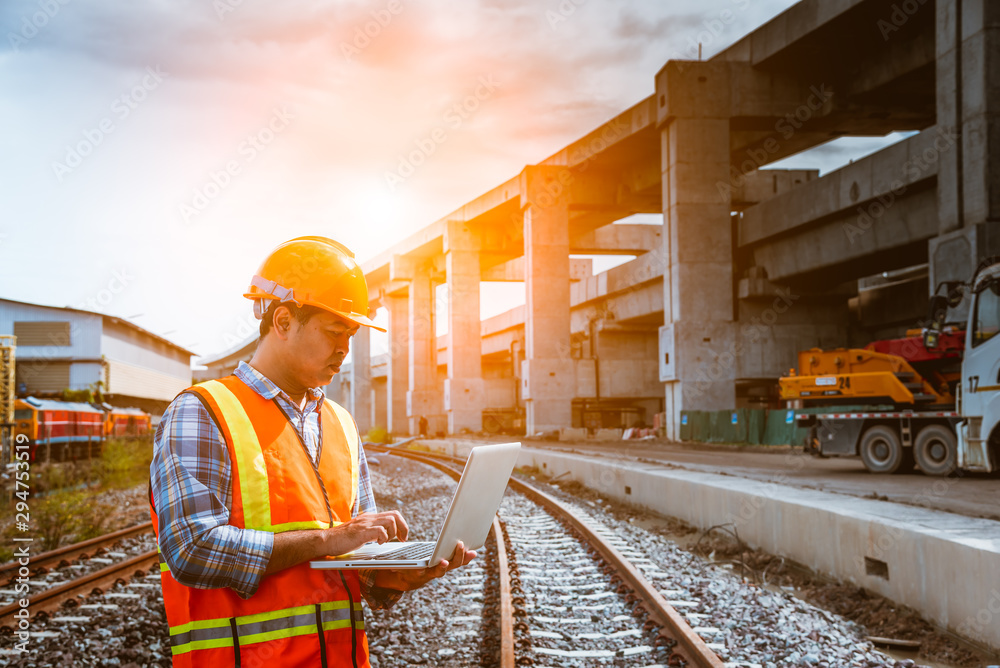 A engineer under inspection and checking construction process railway work on rail train station by Blueprint on hand . Engineer wearing safety uniform and safety helmet in work. A engineer under inspection and checking construction process railway work on rail train station by Blueprint on hand . Engineer wearing safety uniform and safety helmet in work.