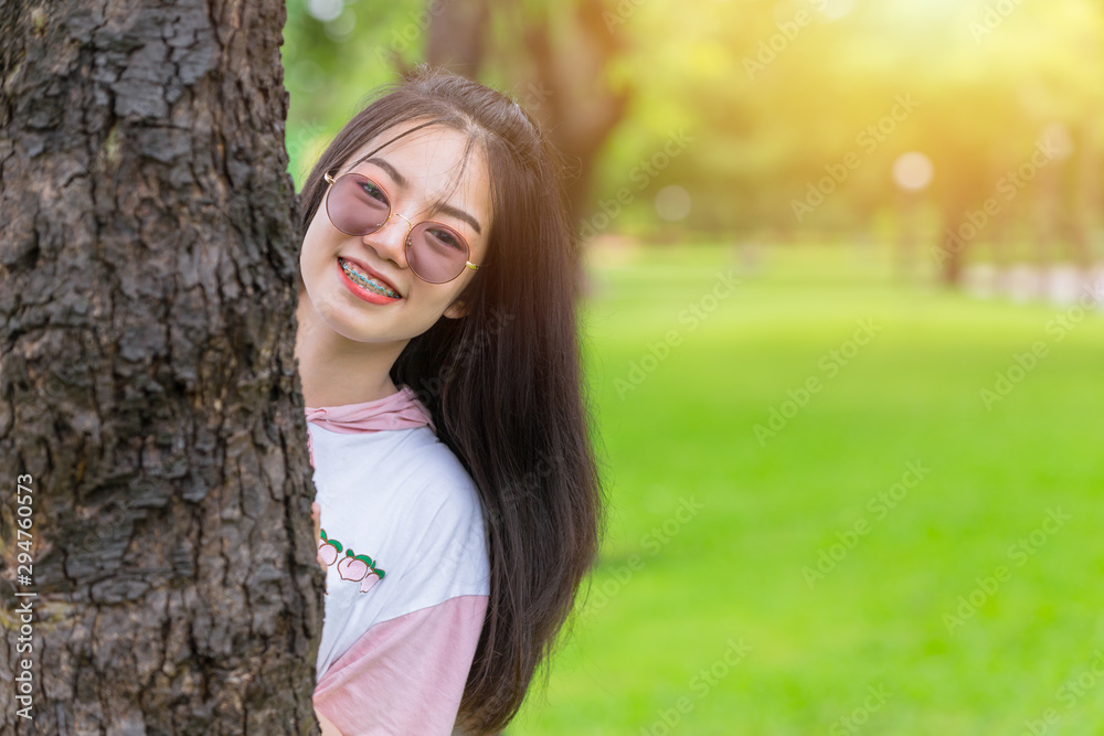 Happy Asian dental braces girl wearing sunglasses happy hide and seek at tree park outdoor portrait. Happy Asian dental braces girl wearing sunglasses happy hide and seek at tree park outdoor portrait.