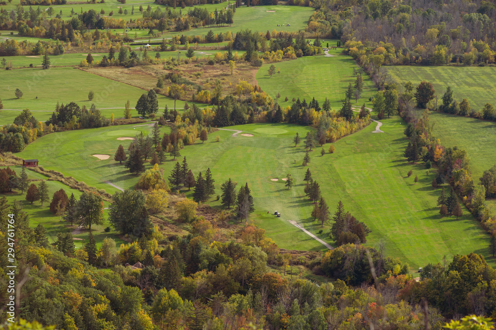Golf course seen from above during autumn, with pine trees and other trees turning red and orange. Quebec, Canada