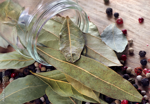 dry bay leaf in a glass jar on a wooden table. bay leaf and pepper mixture close up photo