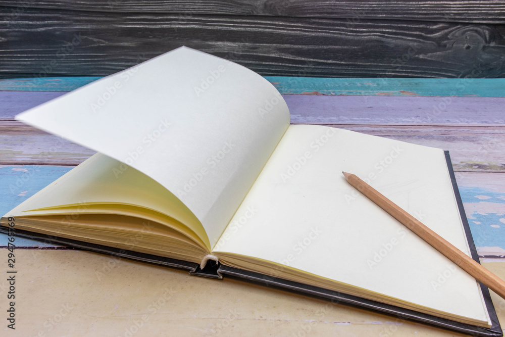 Brown wooden pencil on a notebook placed on an old wooden desk in pastel colors and a black background Brown wooden pencil on a notebook placed on an old wooden desk in pastel colors and a black background