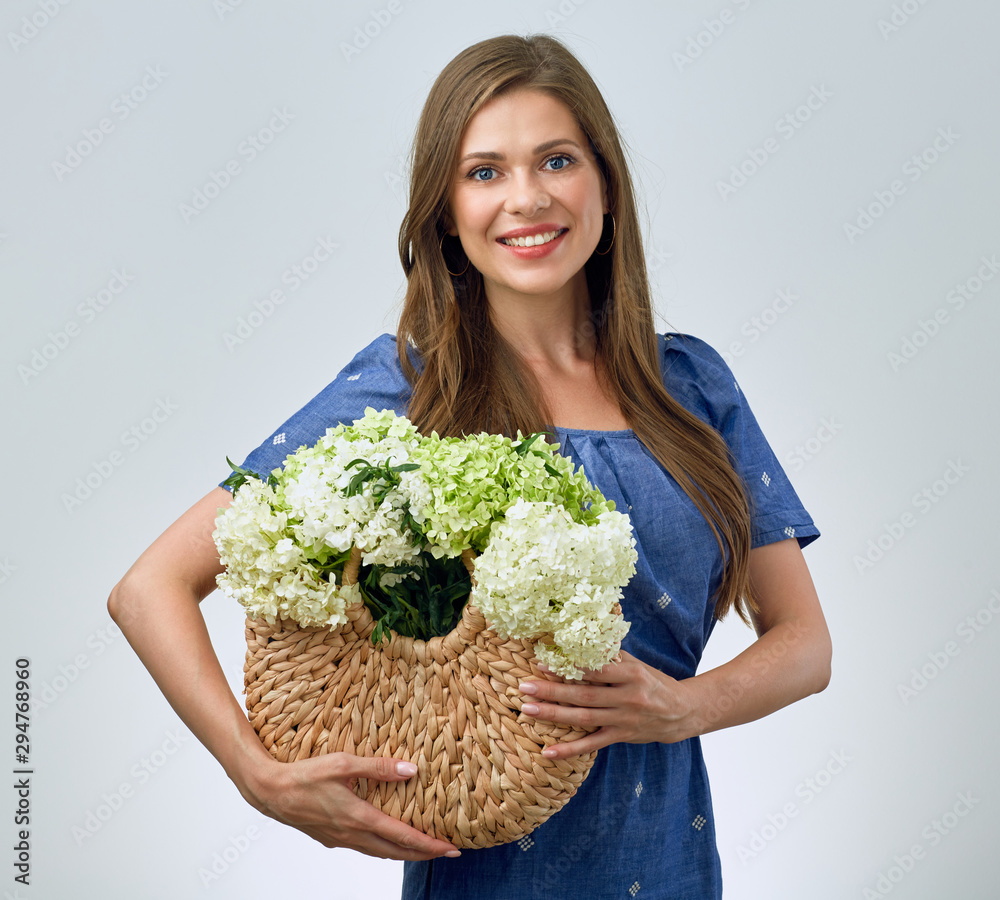 smiling woman holding straw bag with flowers.