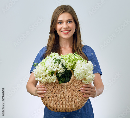 woman holding flowers in straw hand bag.
