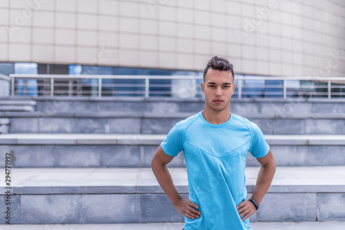 male athlete, in summer city, stands confidently looking, coach controls exercise. Free space for text. Active lifestyle, workout, fitness in fresh air. Motivation for sports. Blue stair t-shirt. © byswat