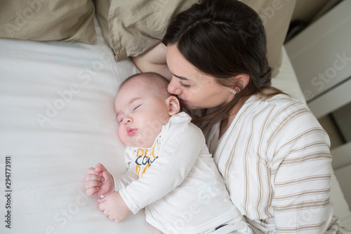 happy young mother kissing her newborn baby sleep in bed. lifestyle mother's day concept