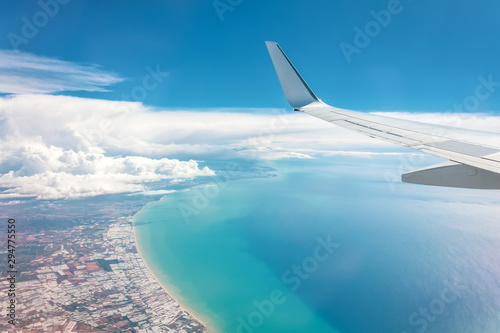 Blue sky high wing view of the sea coast from an airplane, far away white clouds.