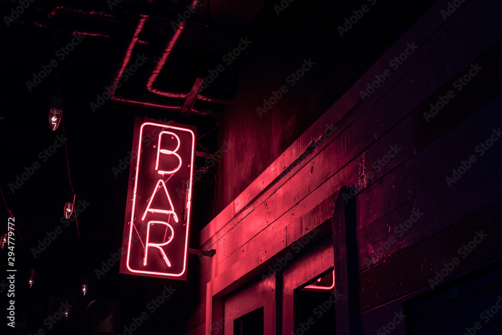neon BAR sign lights up the doorway of a drinking establishment at night - obrazy, fototapety, plakaty 