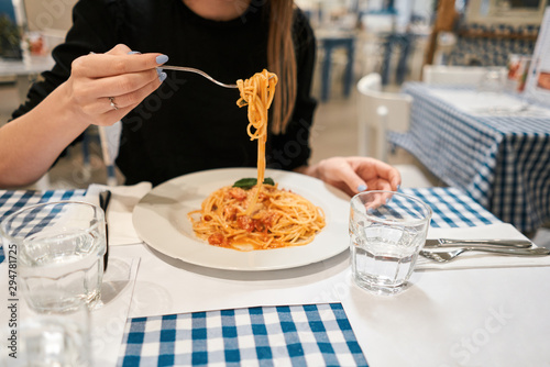 Close-up spaghetti Bolognese wind it around a fork. Parmesan cheese. Young woman eats Italian pasta with tomato, meat. © malkovkosta