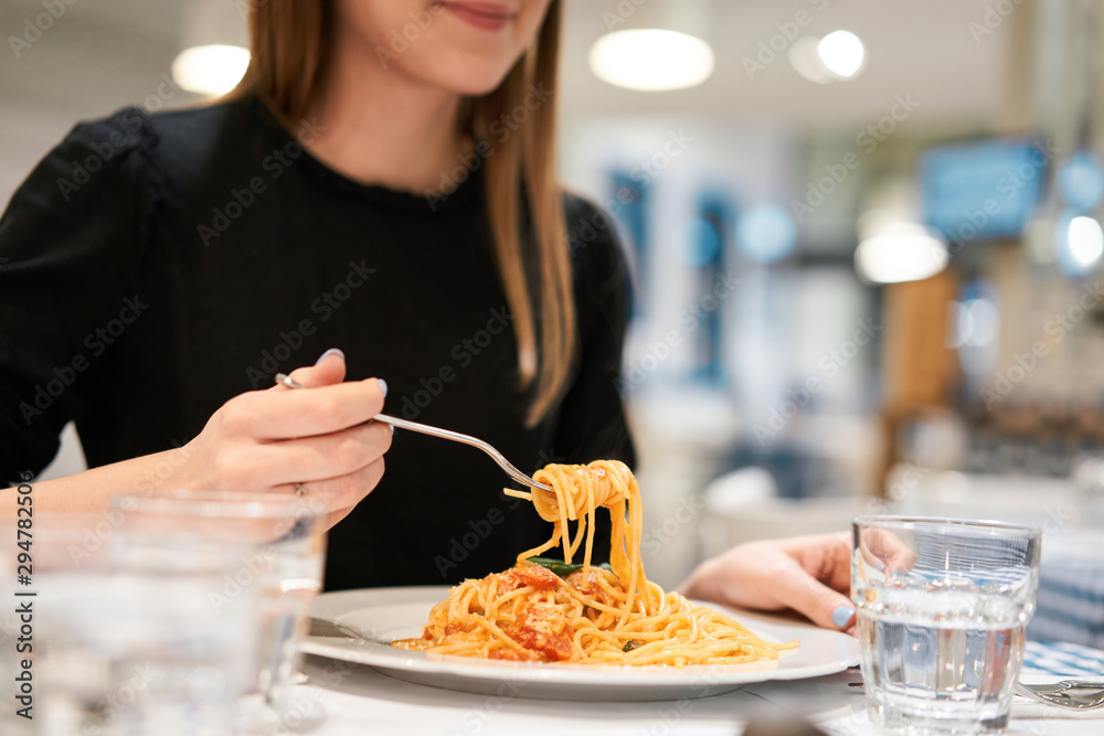 Close-up spaghetti Bolognese wind it around a fork. Parmesan cheese. Young woman eats Italian pasta with tomato, meat.