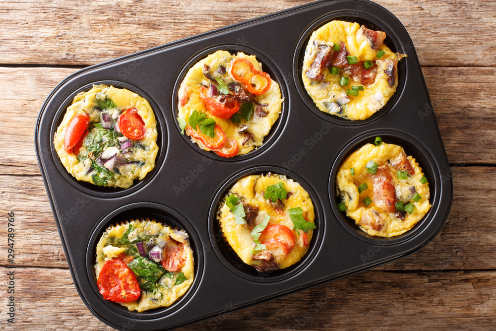 egg muffins omelet with bacon, tomatoes, spinach and mushrooms close-up in a baking dish. Horizontal top view egg muffins omelet with bacon, tomatoes, spinach and mushrooms close-up in a baking dish. Horizontal top view