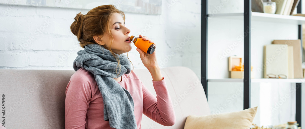 Φωτογραφία panoramic shot of ill woman with grey scarf drinking cough syrup