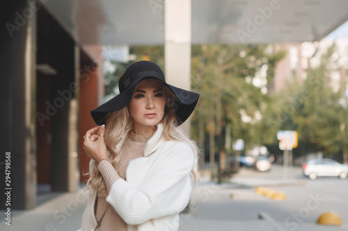 Portrait of a blonde lady in a black hat, long hair, beige coat.