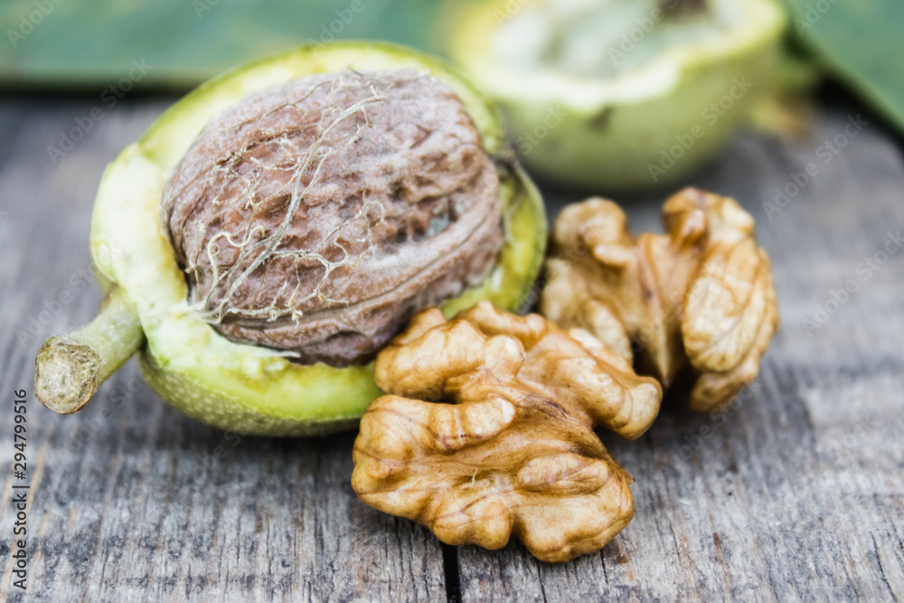 Obraz premium Fresh walnuts in a green shell near the walnut kernel on an old wooden table. Nuts in green shells.