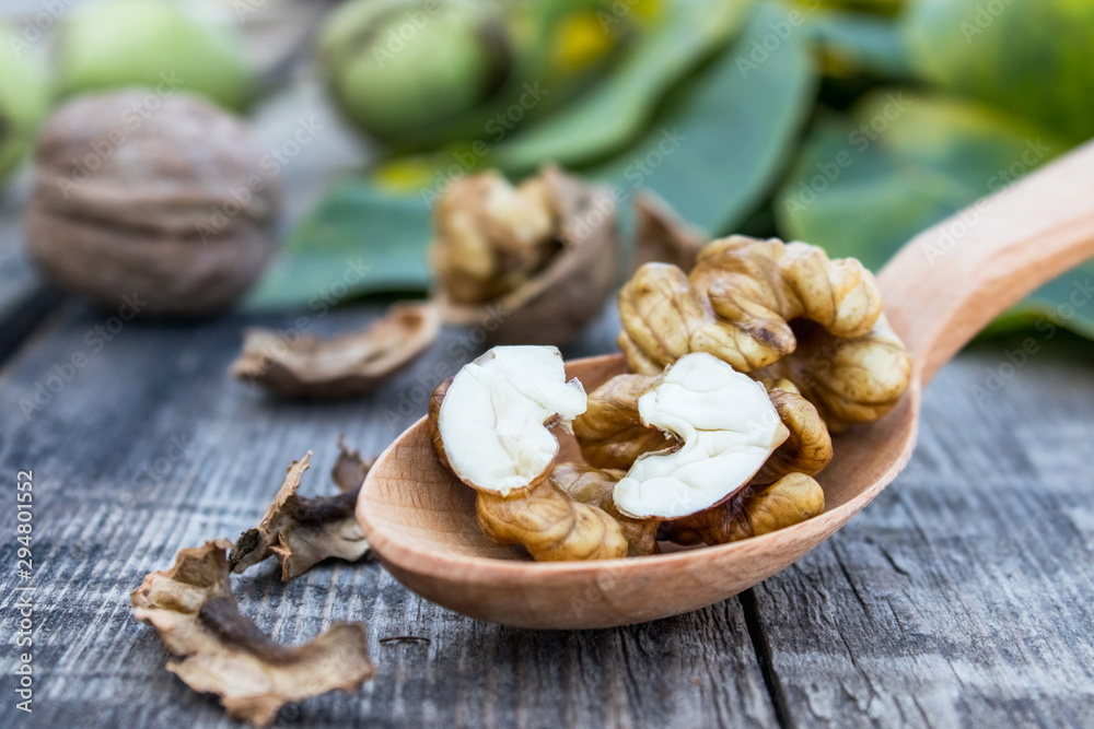 Fototapeta premium Walnuts and walnut kernels lie in a spoon on a rustic old wooden table. Kernels of walnuts.