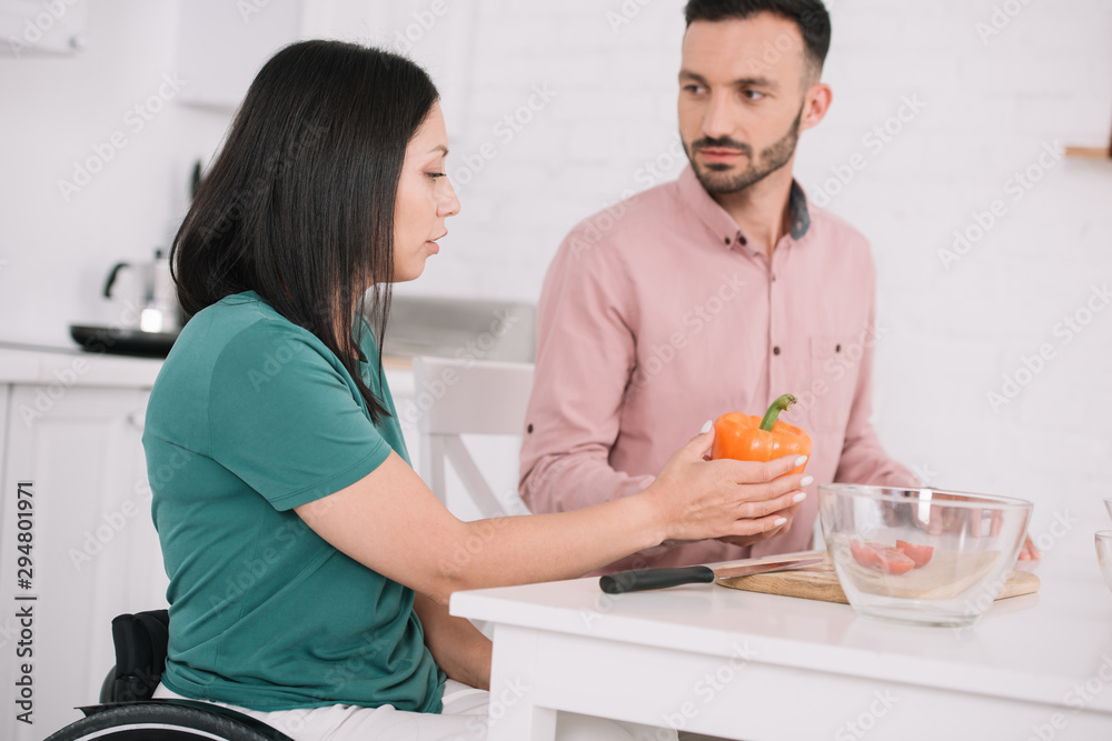 young disabled woman holding bell pepper while talking to boyfriend in kitchen young disabled woman holding bell pepper while talking to boyfriend in kitchen