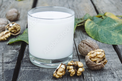 Vegan nut milk in a glass near walnuts on an old wooden table. Vegan milk from walnuts. Eco food.