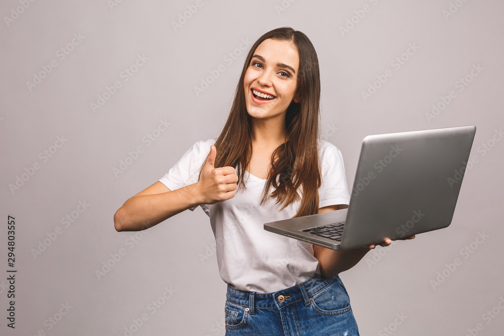 Portrait of a smiling young girl holding laptop computer, thumbs up gesture  isolated over grey background. foto de Stock | Adobe Stock