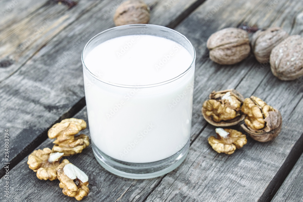 Vegan nut milk in a glass near walnuts on an old wooden table. Vegan milk from walnuts. Eco food. Vegan nut milk in a glass near walnuts on an old wooden table. Vegan milk from walnuts. Eco food.