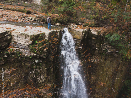man standing on the cliff looking at waterfall autumn time