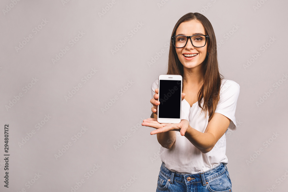 Nice idea! Surprised happy brunette woman showing blank smartphone screen while looking at the camera with open mouth over grey background. Nice idea! Surprised happy brunette woman showing blank smartphone screen while looking at the camera with open mouth over grey background.