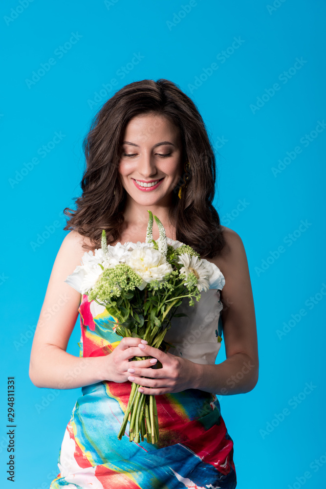 happy elegant young woman in dress holding flowers isolated on blue happy elegant young woman in dress holding flowers isolated on blue