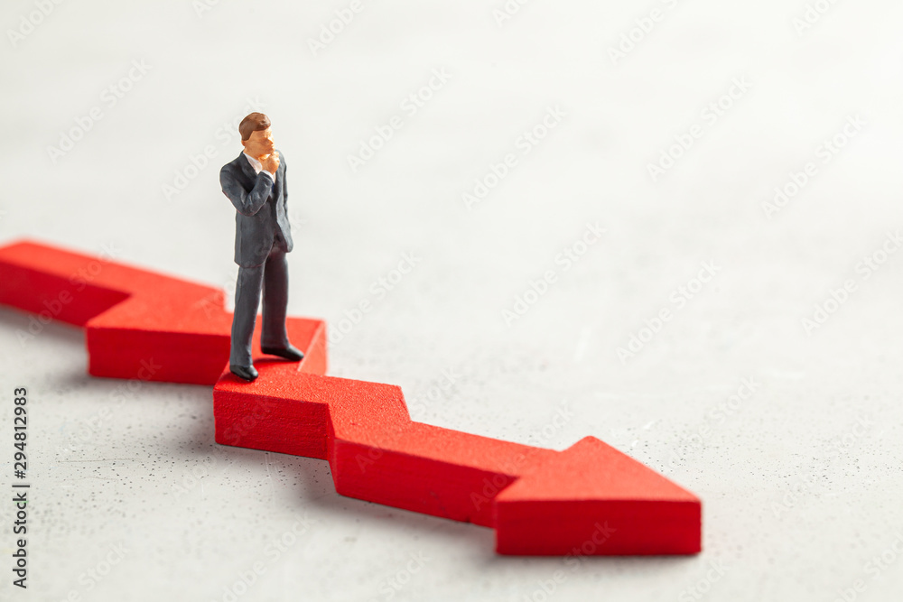 Figurine of a businessman in a suit and tie and a red down arrow. The concept of bankruptcy, falling profits and reducing indicators, analysis of losses. Copy space for text. Figurine of a businessman in a suit and tie and a red down arrow. The concept of bankruptcy, falling profits and reducing indicators, analysis of losses. Copy space for text.