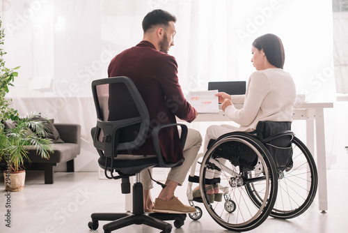 disabled businesswoman in wheelchair showing documents to business partner in office