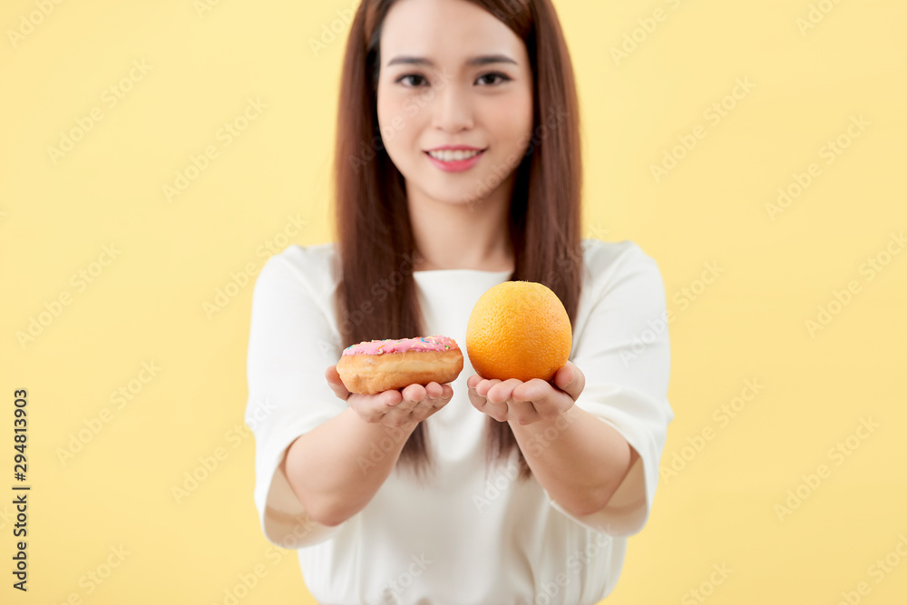 young woman holding donut and orange isolated on yellow background young woman holding donut and orange isolated on yellow background