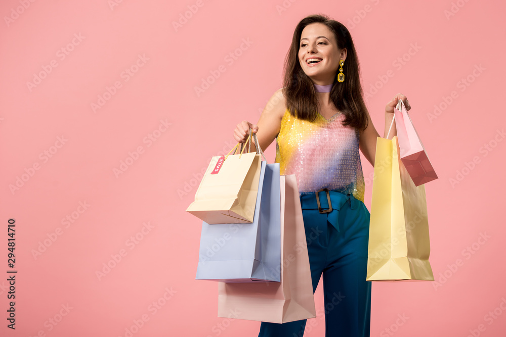 happy stylish disco girl holding shopping bags isolated on pink