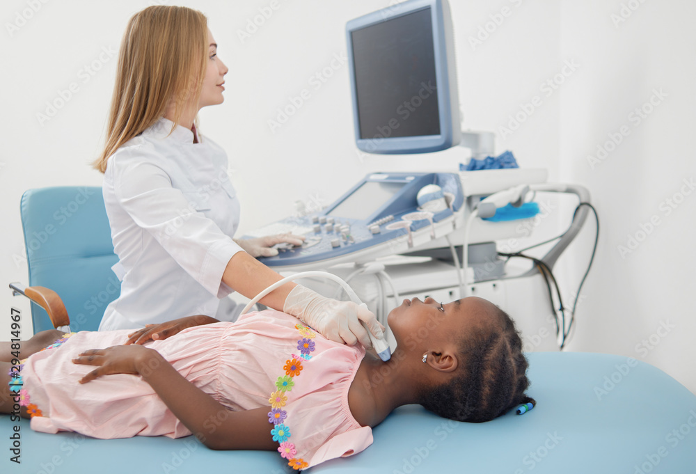 Pretty afro child lying on bed during ultrasound of thyroid. Pretty afro child lying on bed during ultrasound of thyroid.