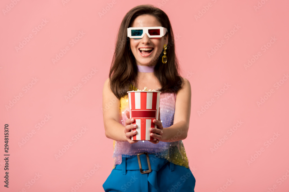 happy young stylish disco girl in 3d glasses holding striped paper bucket with popcorn isolated on pink happy young stylish disco girl in 3d glasses holding striped paper bucket with popcorn isolated on pink