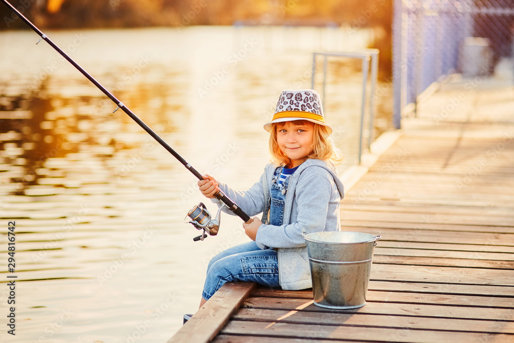 A little girl fishing with a fishing rod from a pontoon or pier on
