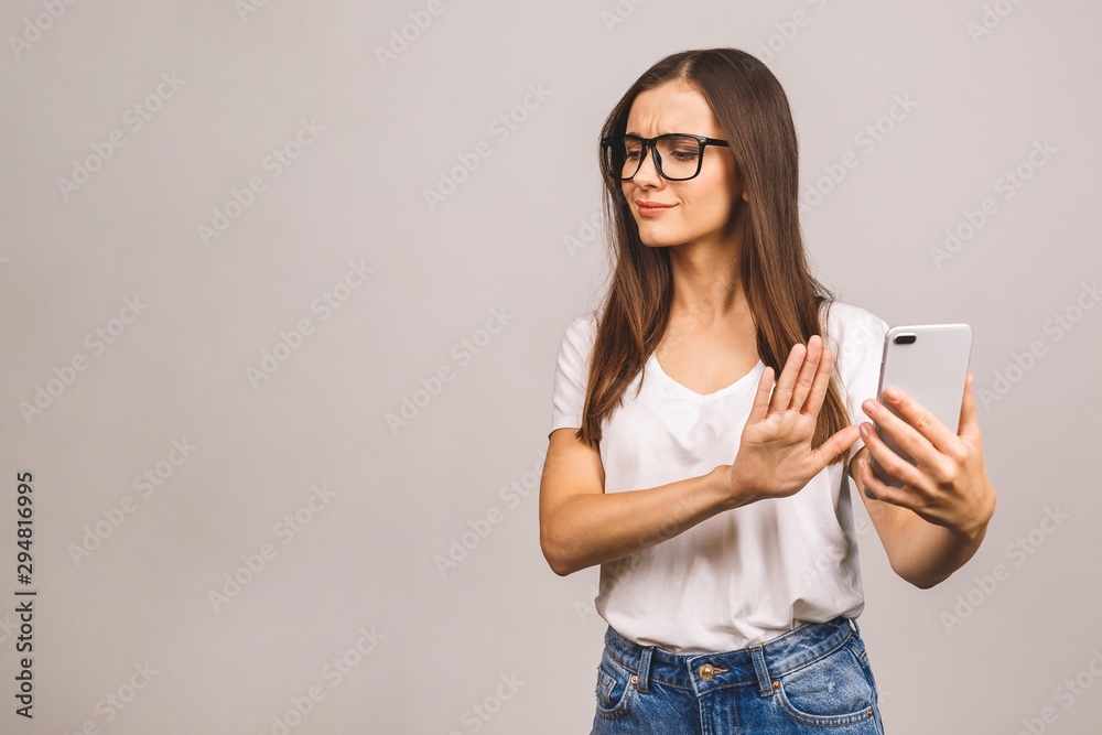 Portrait of a furious sad young woman using mobile phone isolated over grey background. No, stop sign. Portrait of a furious sad young woman using mobile phone isolated over grey background. No, stop sign.