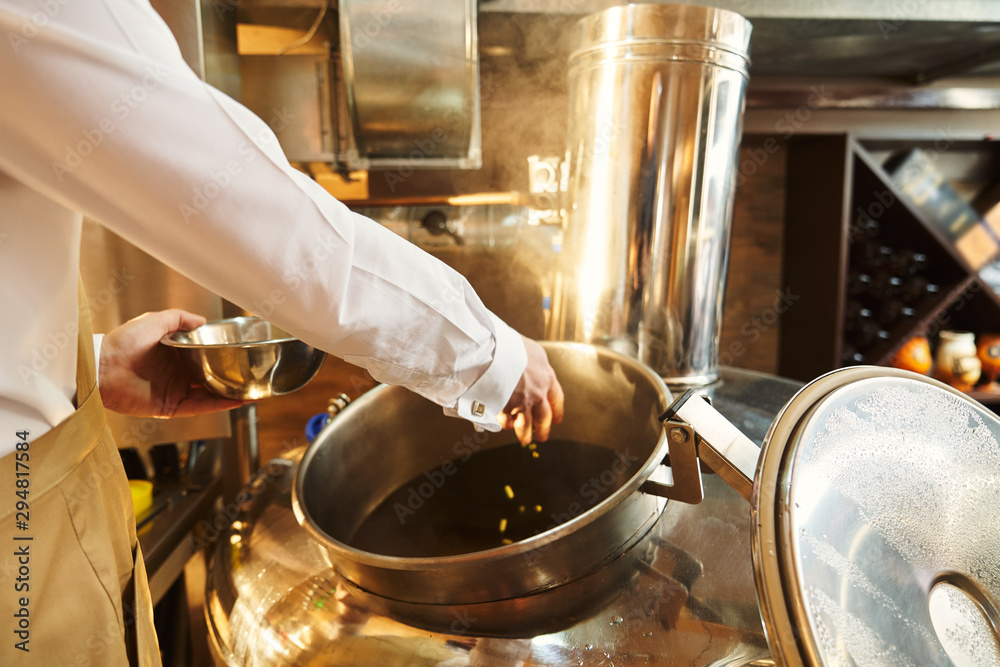 Naklejka premium Brewer adding hops in metallic brew kettle.